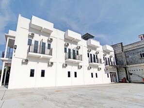 Un bâtiment moderne de couleur blanche, doté de nombreux balcons, de climatiseurs et d’un toit plat.