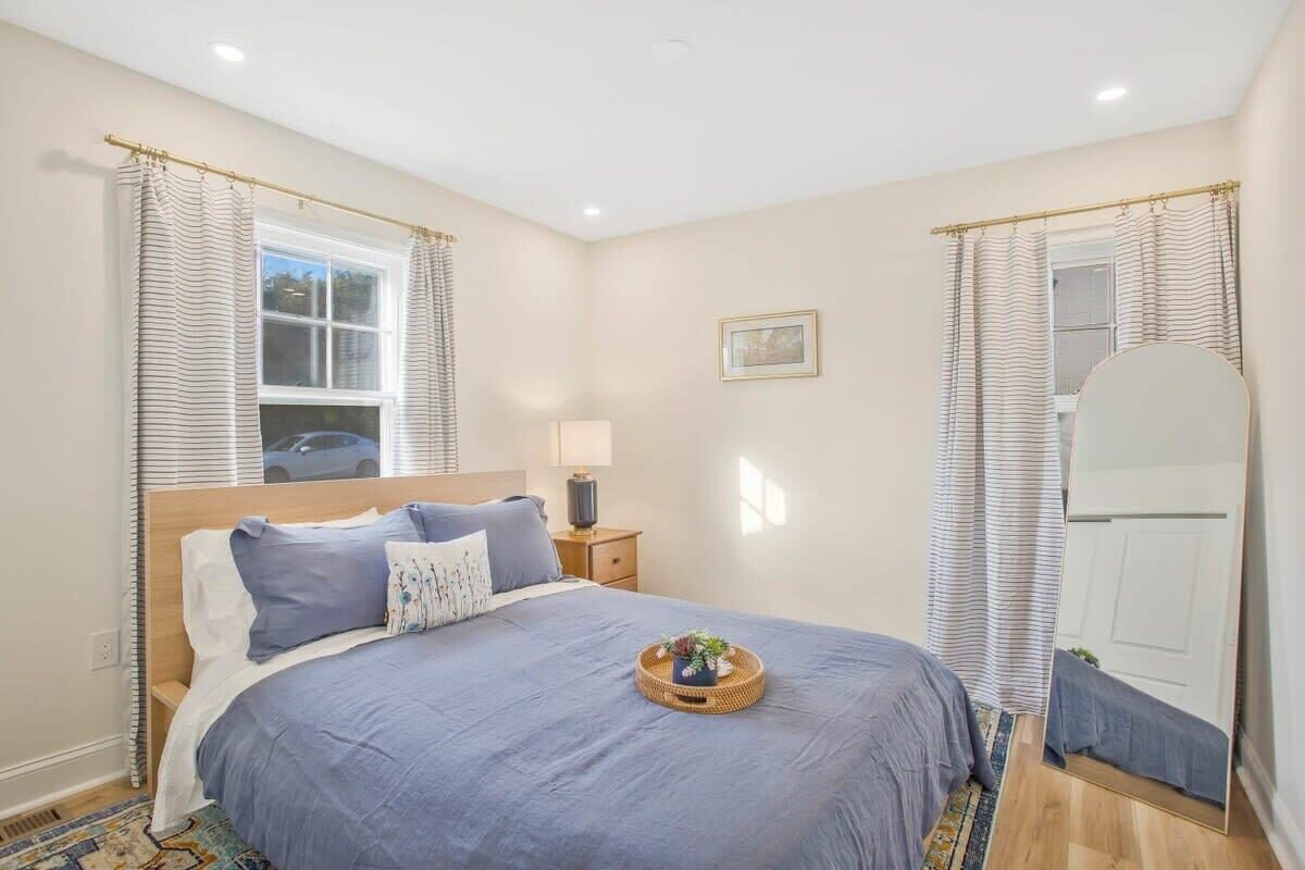 A bedroom with a bed, bedside table, lamp, and a mirror.