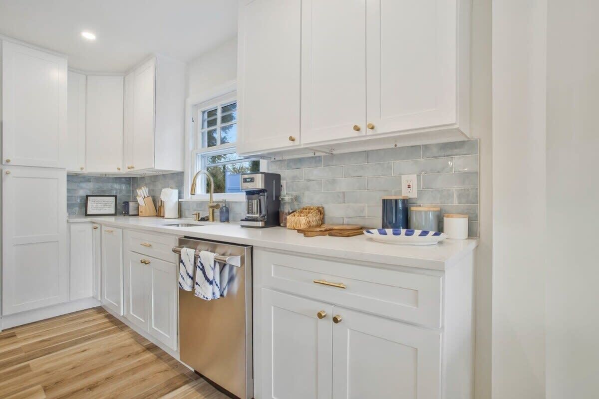 Una cocina moderna con armarios blancos, lavavajillas, cafetera y salpicadero de azulejos.