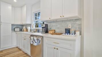 Una cocina moderna con armarios blancos, lavavajillas, cafetera y salpicadero de azulejos.