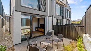 A modern two-story house with a patio area featuring outdoor seating and a fireplace.