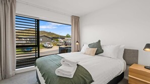 A hotel room with a large bed, a view of the outside, a wooden nightstand, and a lamp.