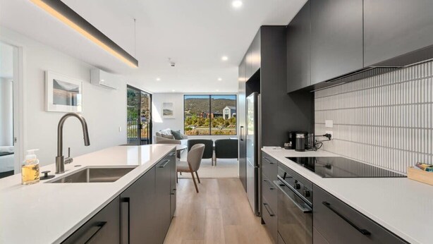 A modern kitchen with a central island, stainless steel appliances, and a view to the outdoors. - Mountain View Apartment Steps from the Village (Wanaka)