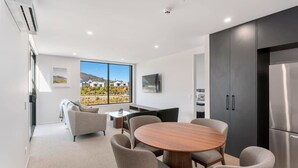 A modern kitchen with a large window, a round dining table, and built-in cabinets. - Mountain View Apartment Steps from the Village (Wanaka)
