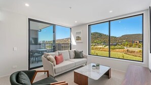 A modern living room with a sofa, a coffee table, and a view of a landscape through large windows. - Mountain View Apartment Steps from the Village (Wanaka)