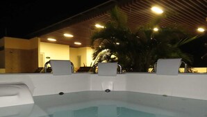 A hot tub area with a pool, surrounded by chairs and palm trees, under a covered roof with lights. - Hotel Cinco Monteria (Montería)
