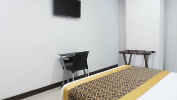 A hotel room with a bed, a desk, and a TV mounted on the wall.
