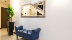 A blue tufted sofa against a white wall with a mirror reflecting a staircase. - Hotel Cinco Monteria (Montería)