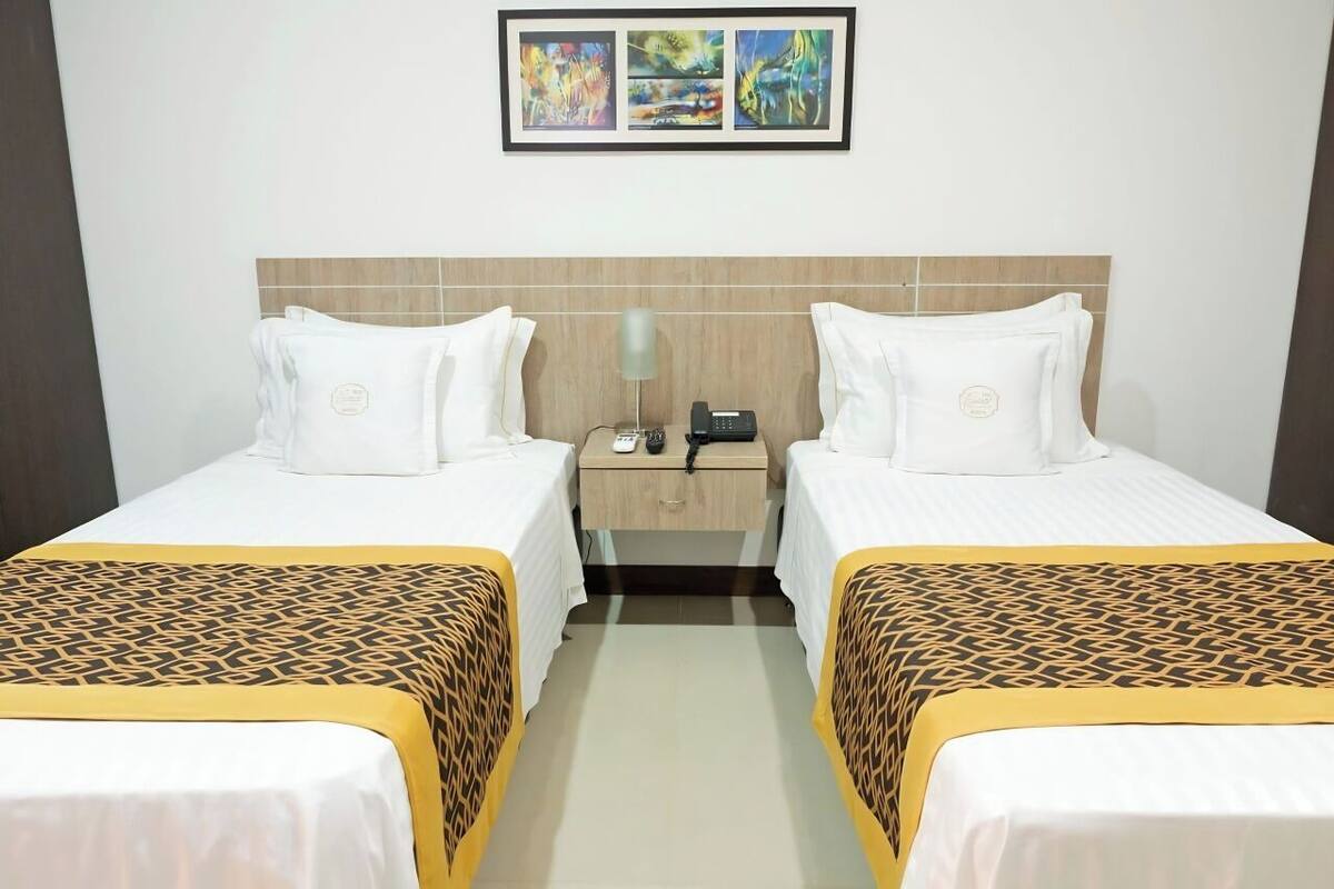 Une chambre d’hôtel avec deux lits simples, une table de chevet avec un téléphone et une œuvre d’art accrochée au mur au-dessus des lits.