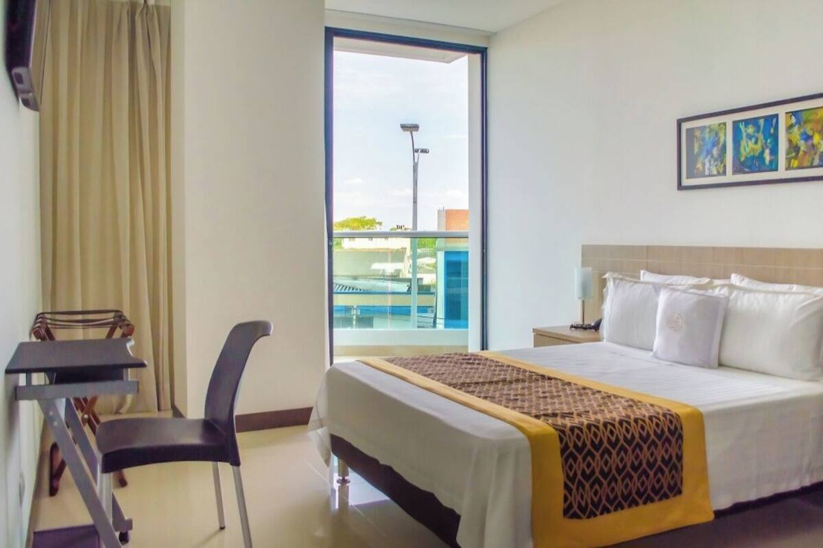 Une chambre d’hôtel comprenant un lit, un bureau, une chaise, une fenêtre donnant sur une piscine et des œuvres d’art accrochées au mur.