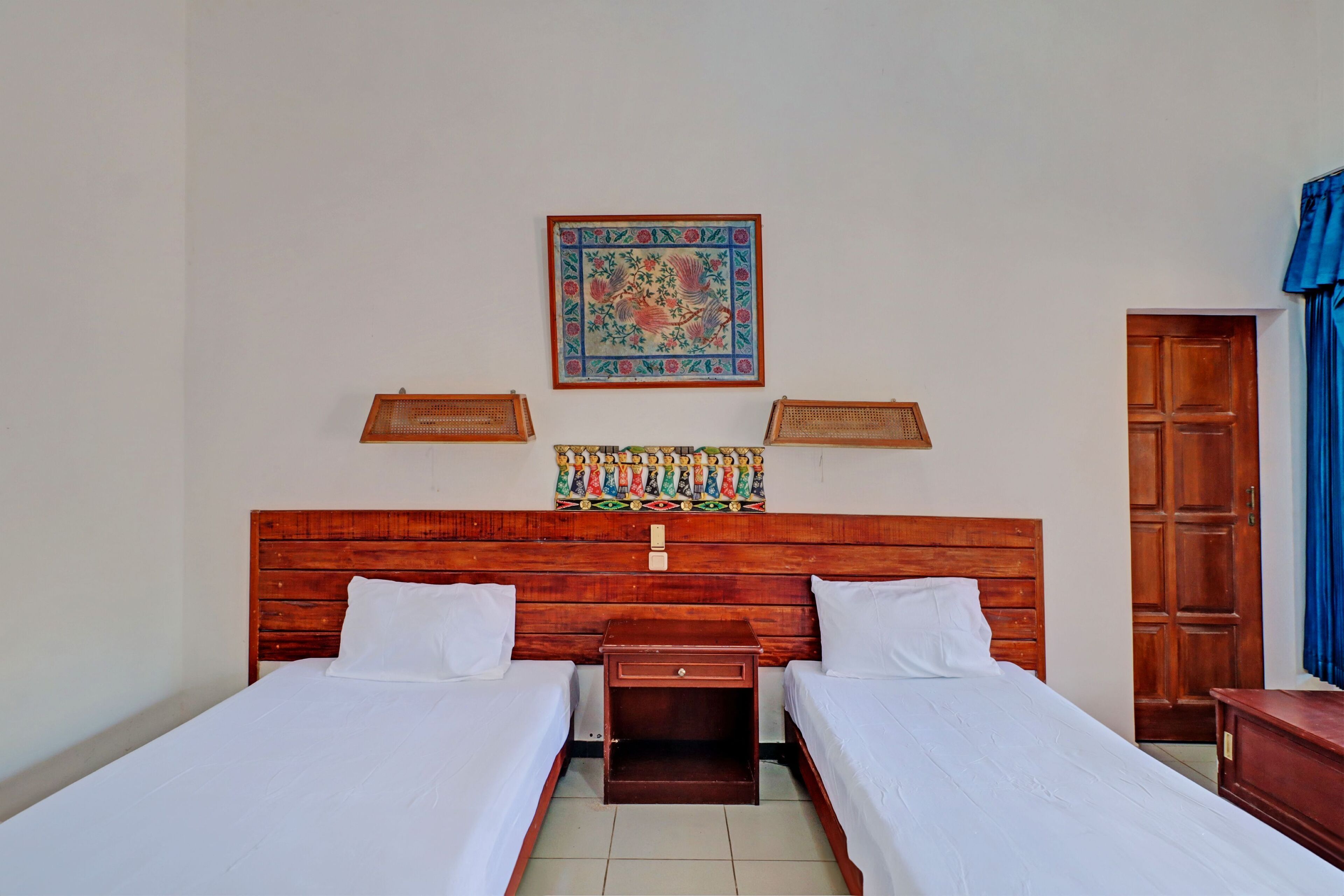 A room with two beds, a wooden headboard, a wall-mounted tapestry, and a wooden wardrobe.