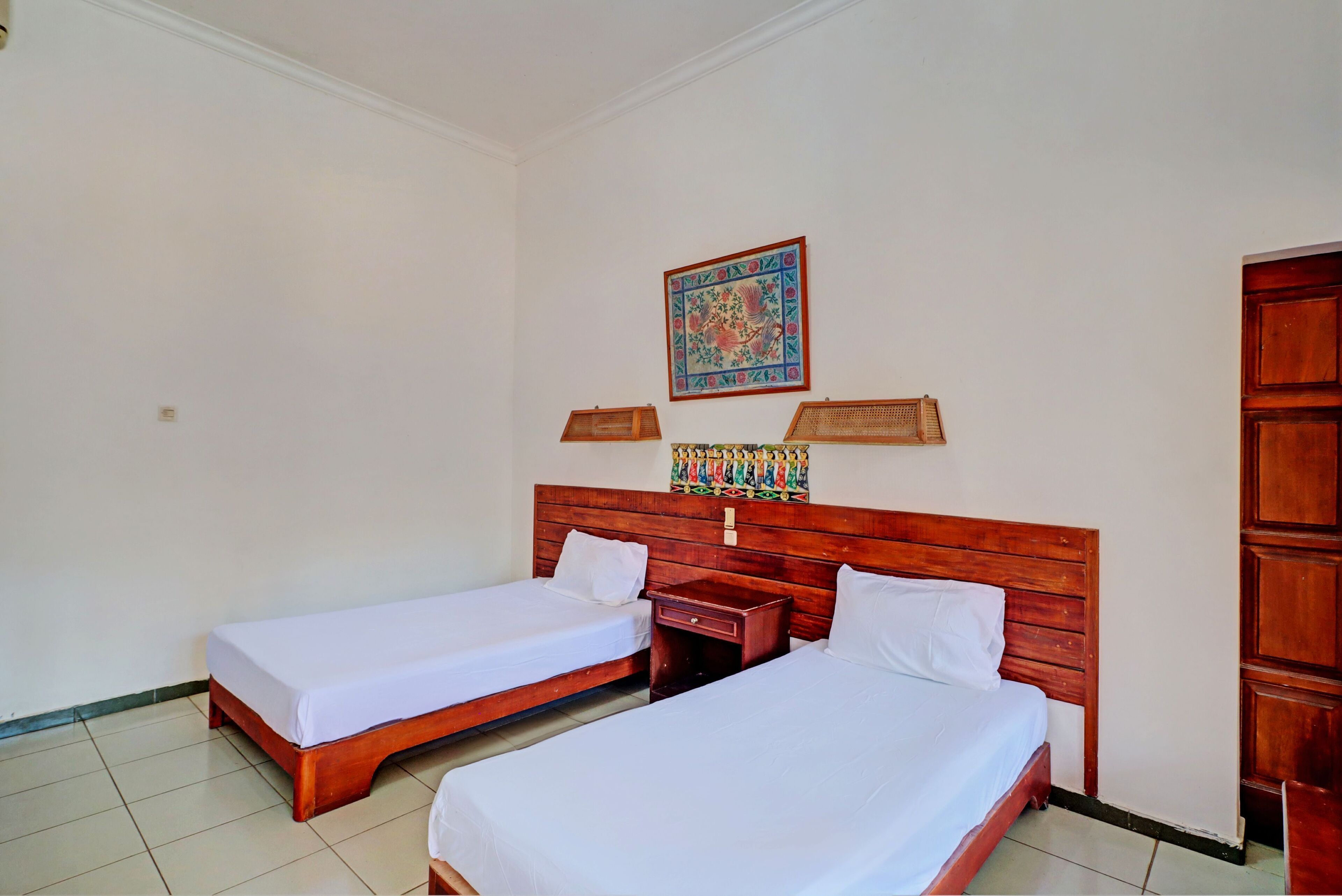 A room with two single beds, a wooden headboard, a small wooden nightstand, and a colorful artwork on the wall.