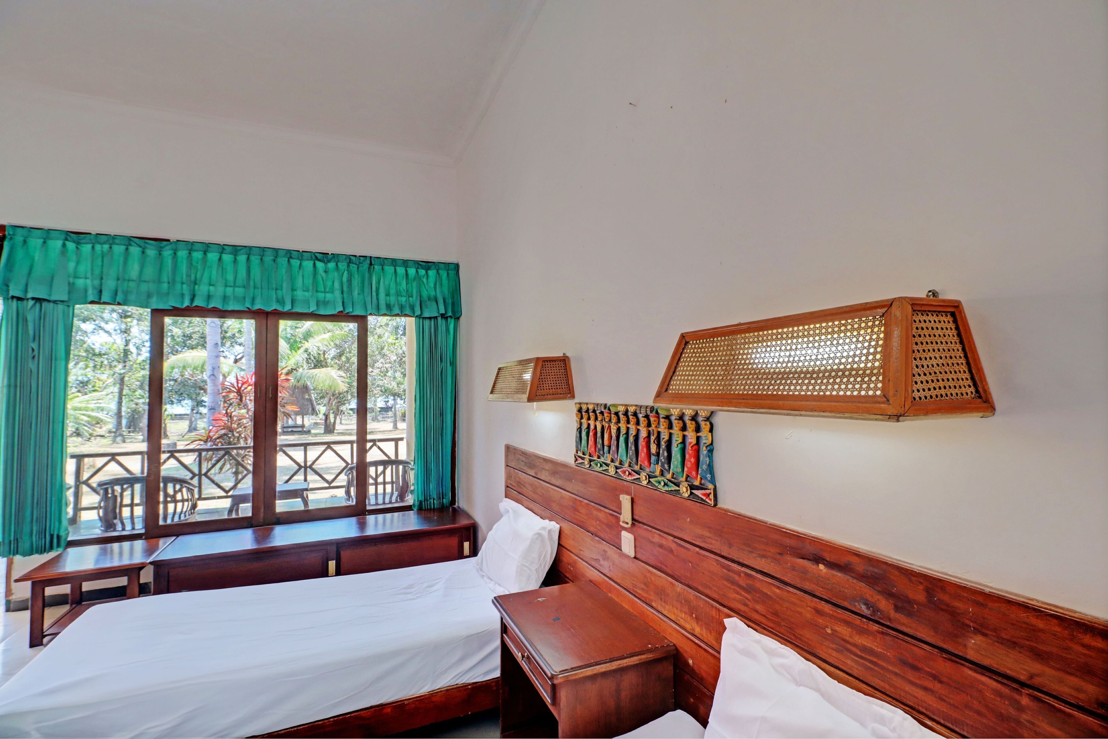 A room with two wooden beds, a bench, a window with curtains, and a rattan headboard.