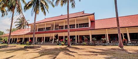 Kaksikerroksinen rakennus, jossa on punainen katto ja valkoiset seinät. Sen ympärillä on palmuja ja nurmialuetta.