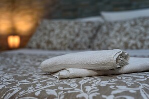 A neatly made bed with a patterned bedspread and rolled white towels. - Via Lubrano 6 in Pozzuoli (Pozzuoli)