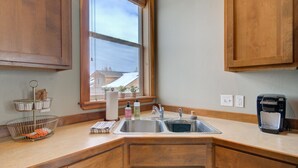 Una cocina con armarios de madera, un fregadero, una cafetera y una ventana con vista a casas.