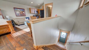 Amplia sala de estar con escalera de madera, cocina con armarios de madera y comedor con mesa y sillas.