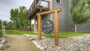 Une pancarte en bois portant les inscriptions « RAILWAY » et « superbe à tous points de vue » est placée devant une maison moderne dotée d’un balcon.