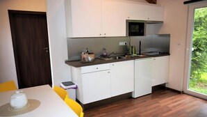 A modern kitchen with white cabinets, a microwave, and a sink. There's a dining table with yellow chairs and a window providing a view of greenery.