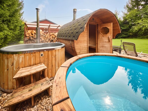 A wooden hot tub and a swimming pool with a wooden deck and seating area.