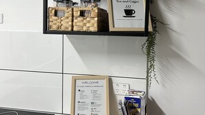 A kitchen with a black shelf holding wicker baskets, a framed sign for complimentary tea and coffee, and a welcome sign for a Norfolk hideaway. - Norfolk Hideaway - Port Macquarie | Easy walk to Ocean and Beaches  (Port Macquarie)