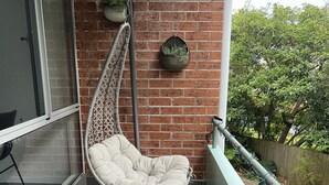 A balcony with a hanging chair, a potted plant, and a pair of shoes on the floor. - Norfolk Hideaway - Port Macquarie | Easy walk to Ocean and Beaches  (Port Macquarie)