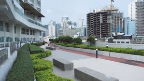 A modern urban landscape with a pedestrian pathway, green landscaping, and high-rise buildings, including a construction site. - The Beacon Makati by mvmtransient (Makati)