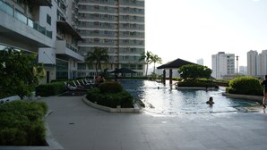 A swimming pool area with a pavilion, palm trees, and a high-rise building in the background. - The Beacon Makati by mvmtransient (Makati)
