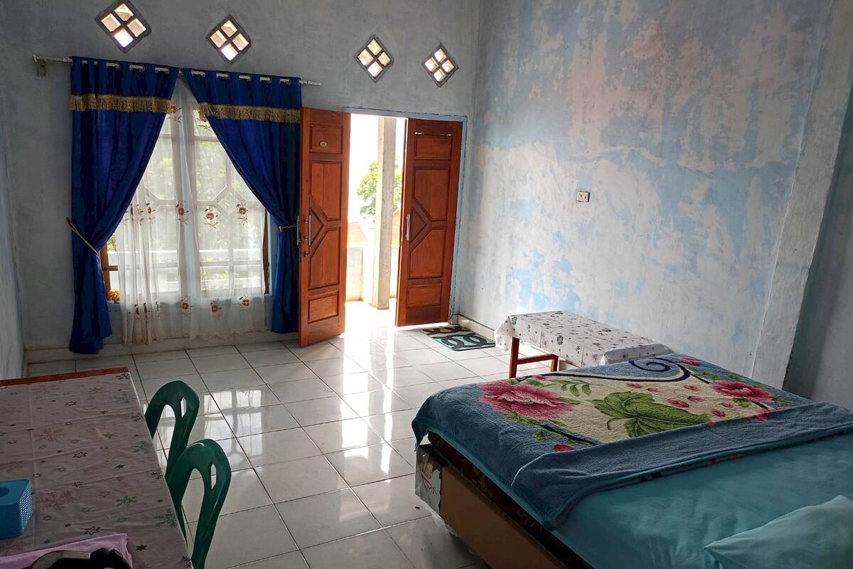 Un dormitorio con cama, una mesa, sillas y un ventanal con cortinas.