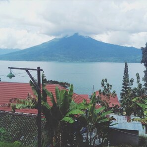 A mountain with a lake in the foreground, surrounded by vegetation and buildings with red roofs.