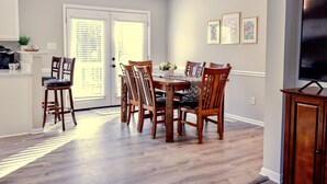 Un coin repas avec une table et des chaises en bois, un lustre et un téléviseur posé sur un meuble.