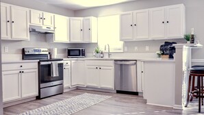 Une cuisine moderne avec des meubles blancs, des appareils en acier inoxydable et un coin bar équipé de tabourets.