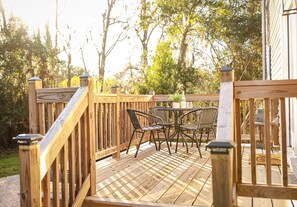 Terraza de madera con una mesa y sillas, rodeada de árboles.