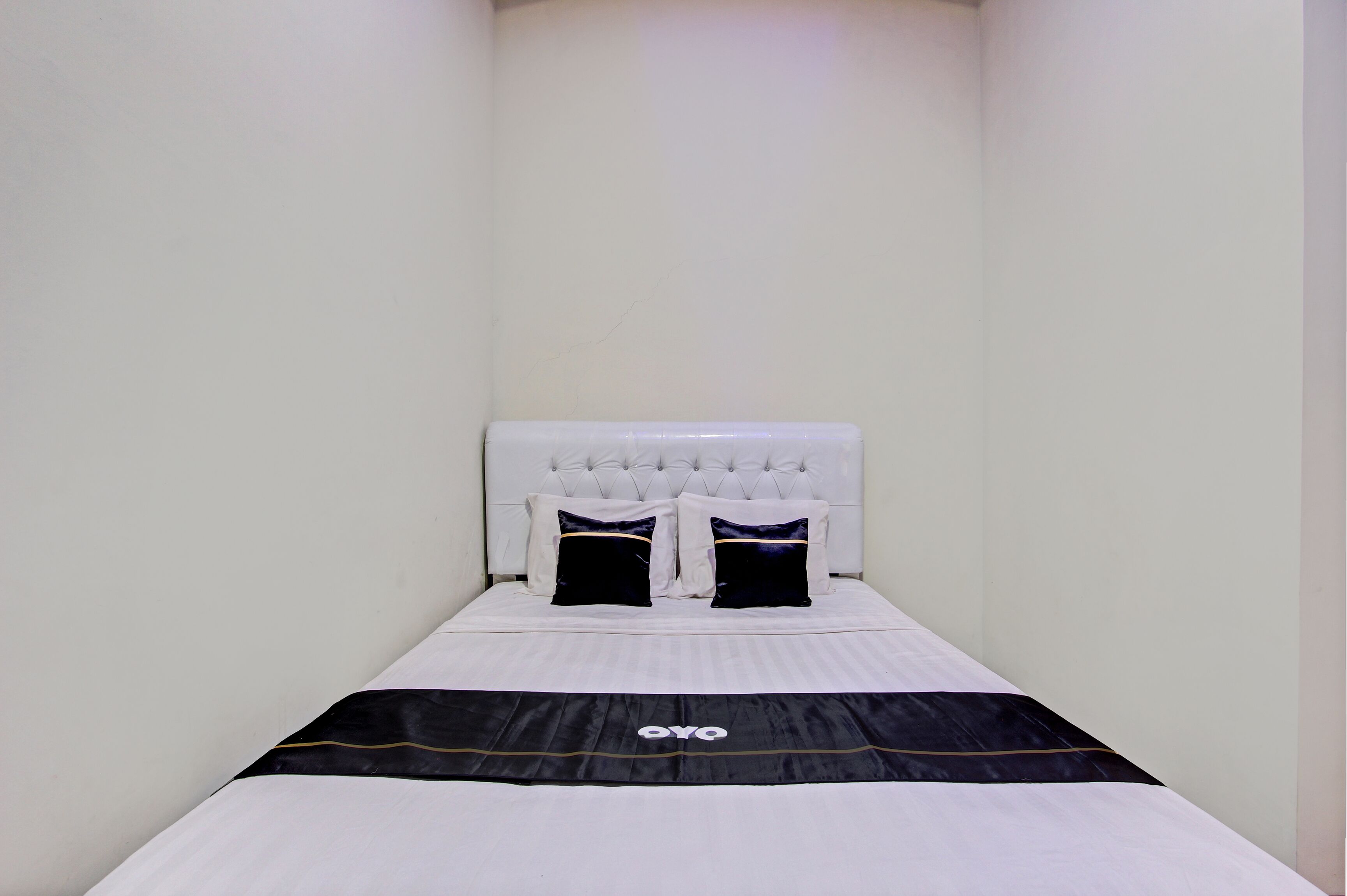 A small, neatly made bed with a white headboard and two black pillows with a galaxy design.