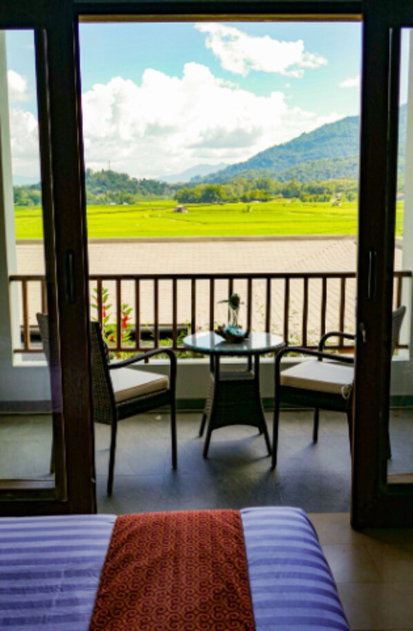 A balcony with a bed, a table, and two chairs. - Santai Toraja (Rantepao)