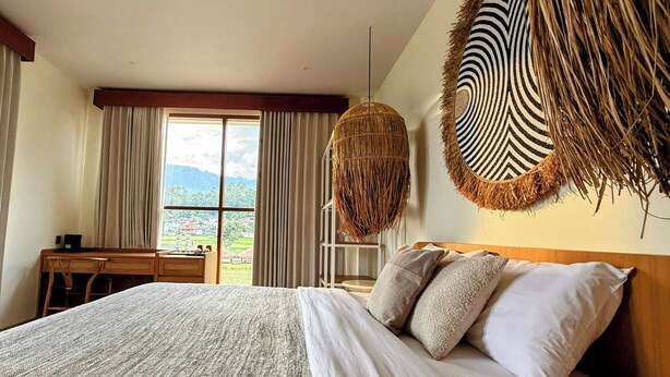 A bedroom with a large bed, a desk, and a view of a landscape. - Santai Toraja (Rantepao)
