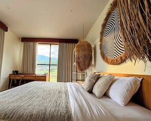 A bedroom with a large bed, a desk, and a view of a landscape. - Santai Toraja (Rantepao)