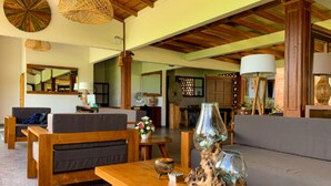 A spacious living area with a wooden coffee table, a sofa, and a dining table. There are woven lampshades and a large mirror on the wall. - Santai Toraja (Rantepao)
