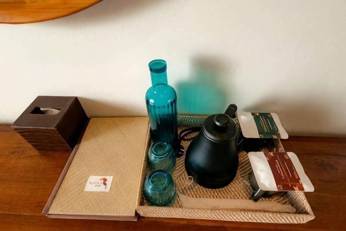 A tray with a black teapot, a blue bottle, and a box of tea on a woven mat.