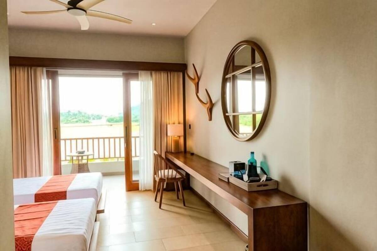 A hotel room with two beds, a desk, a chair, a mirror, and a balcony with curtains.