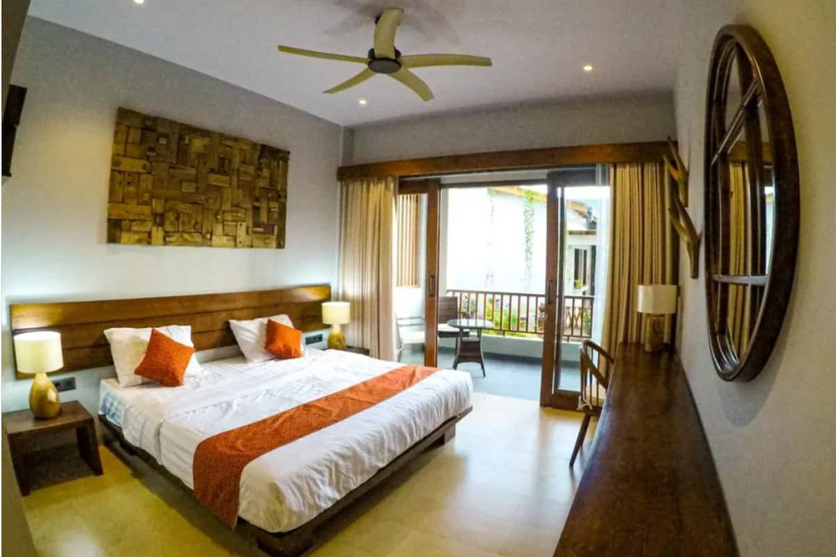 A hotel room with a large bed, a ceiling fan, a balcony with a view, and a wooden headboard.