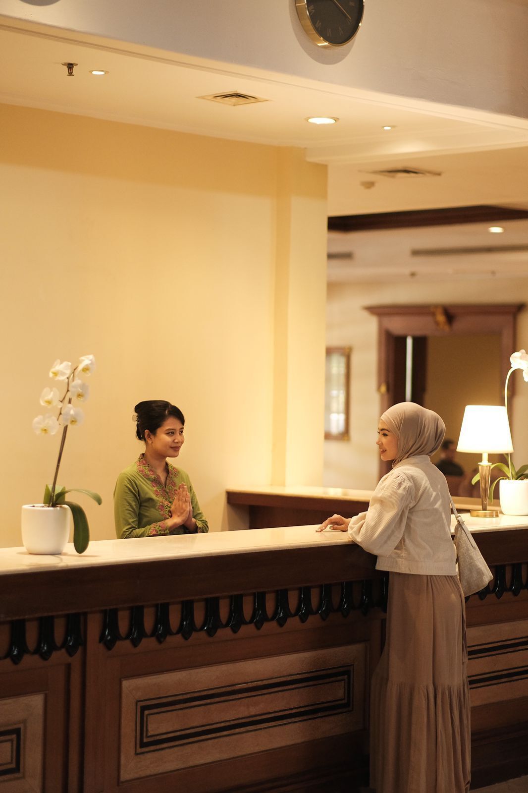 A reception area with a reception desk, a clock, and a potted orchid.