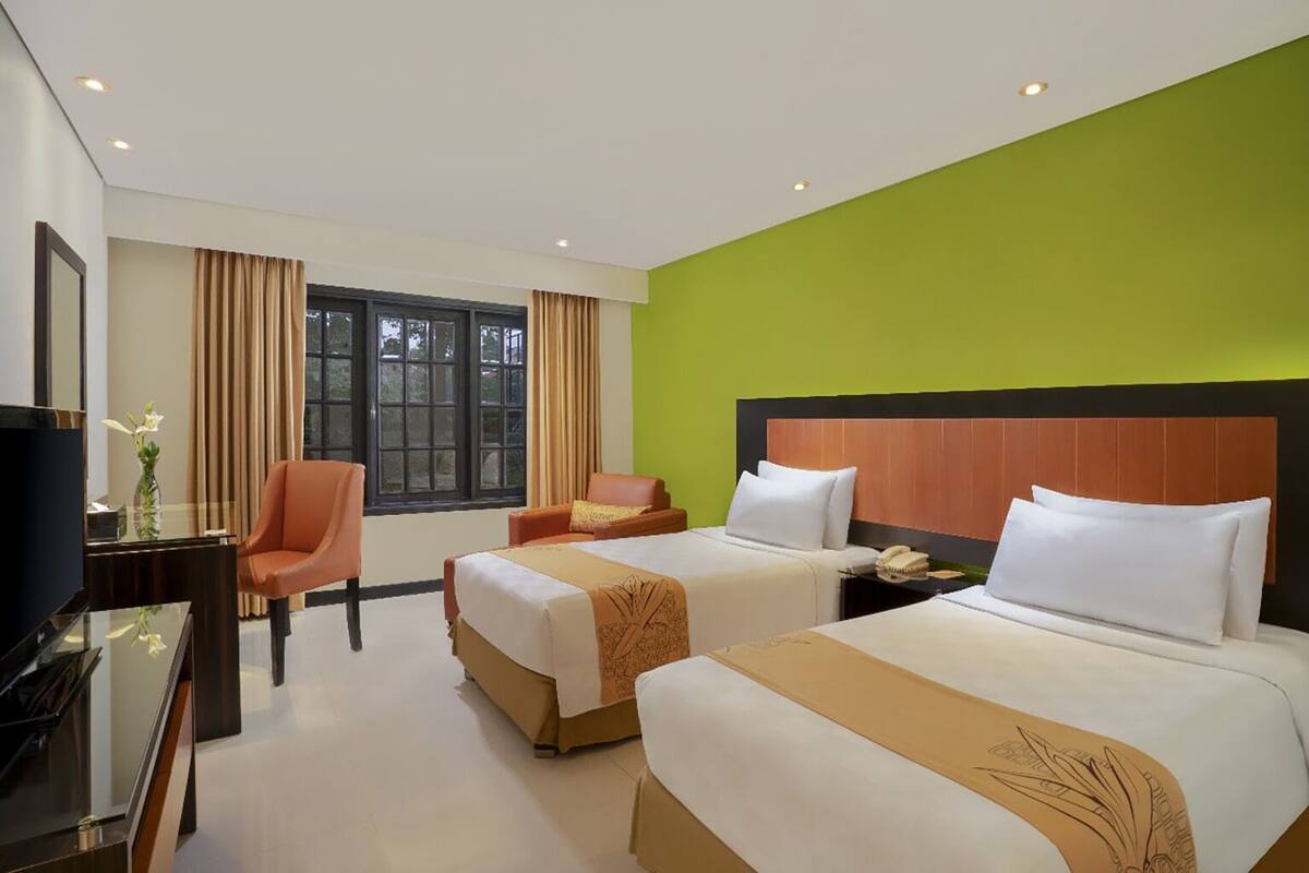 Una habitación de hotel con dos camas, televisión, escritorio y una silla.