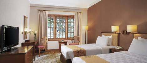 Habitación de hotel con dos camas, un escritorio con televisor, una silla, una mesita y una ventana con cortinas.