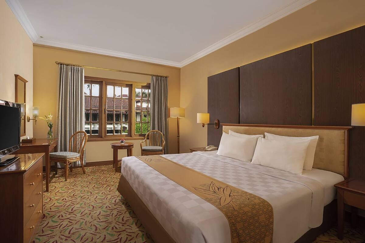 Habitación de hotel con una cama grande, un escritorio con televisor, una silla y una ventana con cortinas.