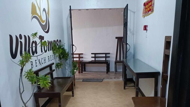 Un área de recepción con el logotipo de Villa Tomasa Beach Resort, un banco, una pequeña mesa y una planta en maceta.