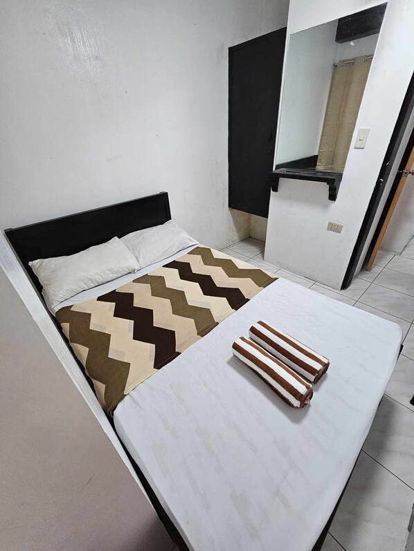 A small, compact bedroom with a bed, a bedside table, and a mirror.