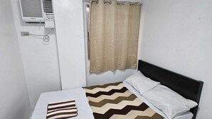 Una cama individual con un almohadón a rayas, una cortina color beige y un aire acondicionado instalado en la pared.
