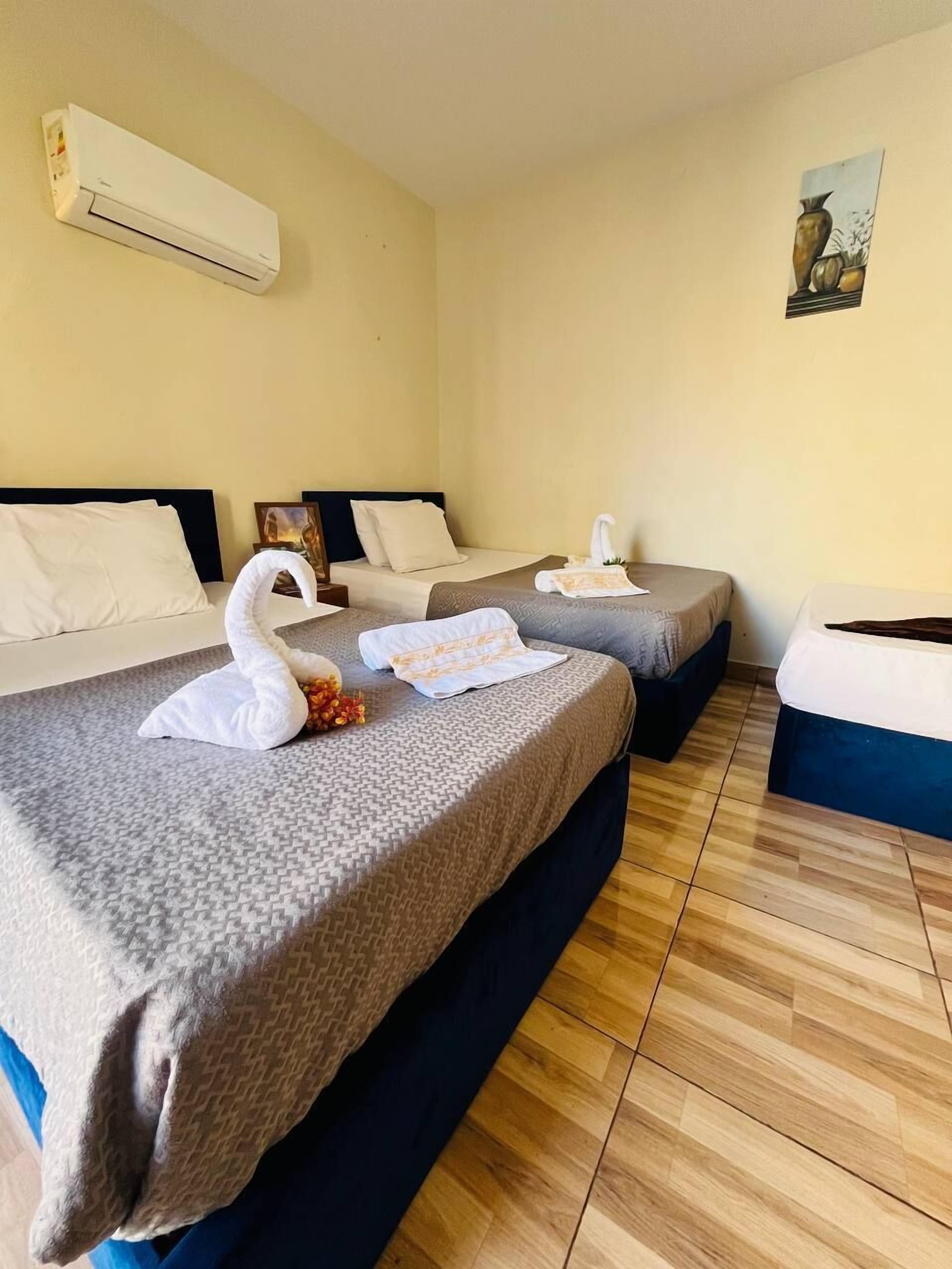 A hotel room with two beds, a painting on the wall, and an air conditioning unit.