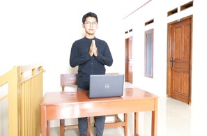 A person standing at a wooden table with a laptop, in a room with wooden doors and a radiator. - Hotel O Wisma Jasmine Syariah (Kuningan)